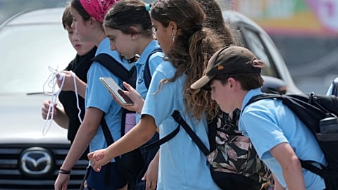 A school girl uses her phone as she walks with a group of kids in Sydney, Monday, Dec. 8, 2025.