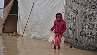 يحمل طهريّر الرواّغ، 8 أعوام، كيساً بلاستيكياً يحتوي على الخبز، بينما ينظر حوله وهو واقف في منطقة غارقة بالمياه داخل مخيم خيام مؤقت، بعد هطول أمطار غزيرة في دير البلح