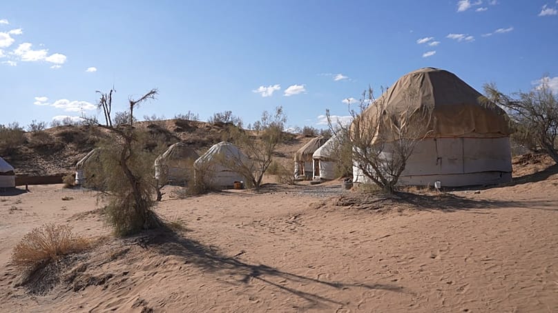 A cluster of traditional yurts set against the sandy landscape of the Kyzylkum desert in Uzbekistan
