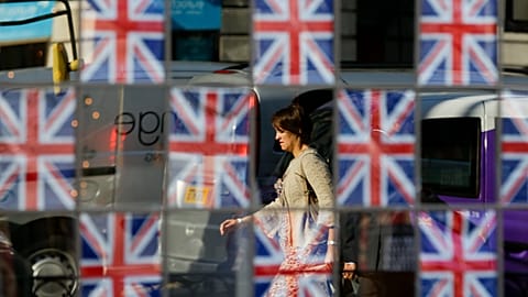 A commute is seen reflected in the glass of a pub window covered in British flags in London. 23 July 2012.