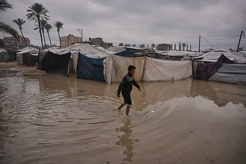 A Palestinian youth walks through a flooded area in a temporary tent camp after heavy rainfall in Deir al-Balah, central Gaza Strip, Friday, Dec. 12, 2025.