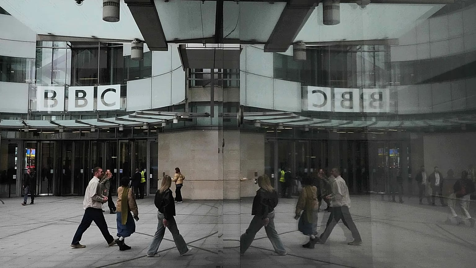 Pedestrians are reflected as they walk outside BBC Broadcasting House in London, 11 November, 2025