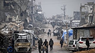 Filistinliler, 15 Aralık 2025 Pazartesi günü Gazze Şehrinde yağmur altında savaşta hasar görmüş binaların sıralandığı bir caddede yürüyorlar.