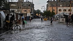 يمشي فلسطينيون في شارع غمرته المياه بعد هطول أمطار غزيرة في دير البلح، وسط قطاع غزة، يوم الثلاثاء 25 نوفمبر 2025.