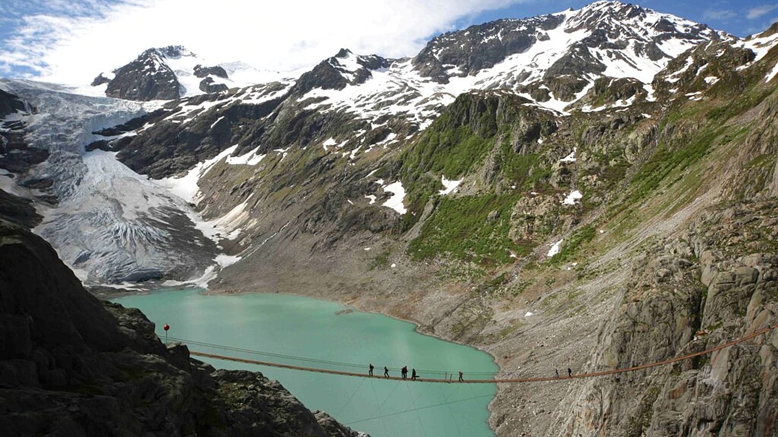 متنزهون يعبرون جسر تريفت الذي أُعيد افتتاحه فوق بحيرة تريفت قرب نهر تريفت الجليدي في وسط سويسرا، في 20 نوفمبر 2025.