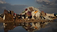 Un garçon palestinien se tient près de sa mère qui fait la lessive, tandis que des matelas, suspendus au-dessus de leur tente, sèchent dans un camp de fortune.