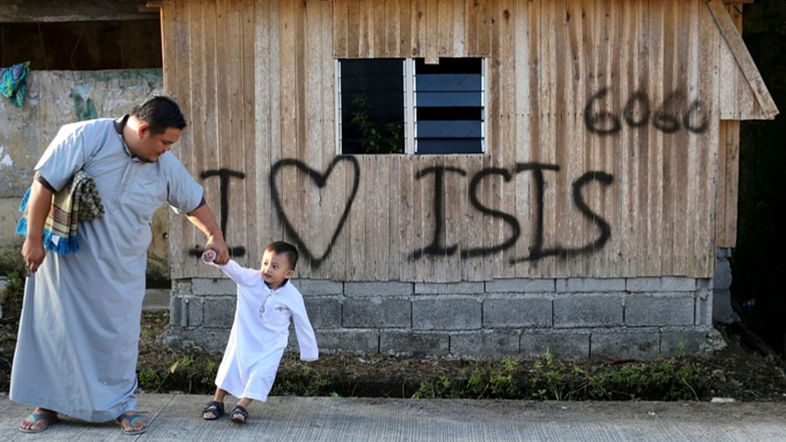 مردی به همراه پسرش از کنار تابلوی «من عاشق داعش هستم» که توسط افراط‌گرایان اسلامی که شهر را تصرف کرده بودند، به جا مانده است، عبور می‌کنند. جنوب فیلیپین، ۲۰۱۸