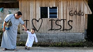 مردی به همراه پسرش از کنار تابلوی «من عاشق داعش هستم» که توسط افراط‌گرایان اسلامی که شهر را تصرف کرده بودند، به جا مانده است، عبور می‌کنند. جنوب فیلیپین، ۲۰۱۸