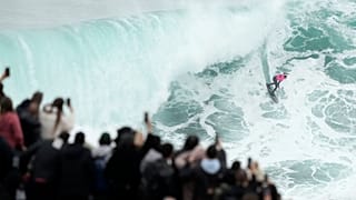 Uma multidão no topo de um penhasco observa um surfista durante o torneio Big Wave Challenge na Praia do Norte, na Nazaré, Portugal