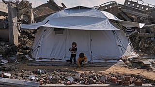 يقف أطفال فلسطينيون أمام خيمة نُصبت في منطقة تحيط بها مبانٍ مدمّرة جرّاء العمليات الجوية والبرية الإسرائيلية في مدينة غزة، الأربعاء 17 كانون الأول/ديسمبر 2025.