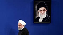 حسن روحانی در حال عبور از کنار تصویر علی خامنه‌ای 