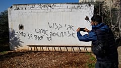 یک مرد فلسطینی از یک گرافیتی به زبان عبری عکس می گیرد که در جریان حملۀ مهاجران اسرائیلی ساخته شده است.