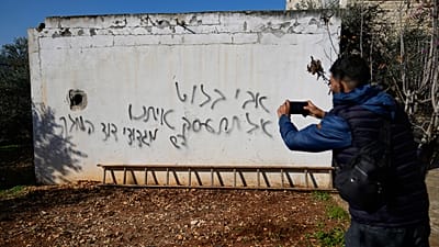 A Palestinian man takes a picture of a graffiti in Hebrew that was made during an Israeli settlers rampage.