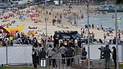 Biztonságiak gyülekeznek a Sydney-i Bondi Beach egyik kapujánál a 2025. december 21-i Bondi lövöldözés áldozatainak és túlélőinek nemzeti emléknapja alkalmából tartott ünnepség előtt.