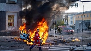 عامل يسير بجانب سيارة مشتعلة بعد هجوم روسي في كييف بأوكرانيا، يوم الاثنين 10 أكتوبر/تشرين الأول 2022.