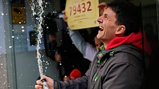 Un hombre descorcha una botella de champán frente a la administración de lotería