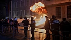 Полицейские наблюдают за тем, как в офис премьер-министра Албании бросают бомбу во время столкновений на антиправительственной демонстрации в столице Тиране, 22 декабря 2025 года.