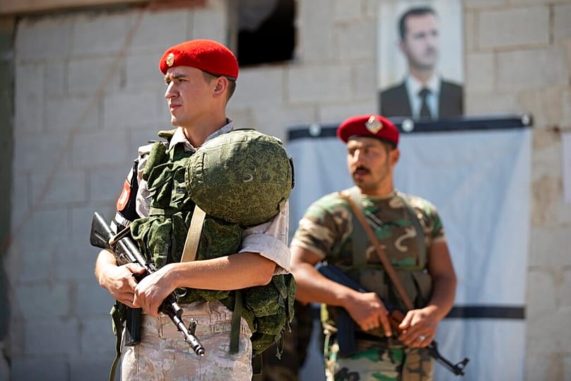 عناصر من الشرطة العسكرية الروسية والسورية (سابقًا)، وخلفهم صورة لبشار الأسد، خلال تدقيق أوراق عائدين إلى البلدة بعد سيطرة القوات الحكومية السابقة عليها، في 25 سبتمبر 2019.