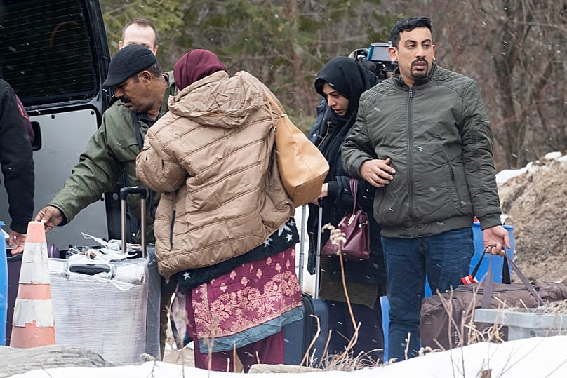 طالبو لجوء ينزلون أمتعتهم من سيارة أثناء انتظارهم دخول كندا عبر طريق روكسهام على الحدود الكندية الأمريكية في منطقة هيمينغفورد، في 25 مارس 2023.