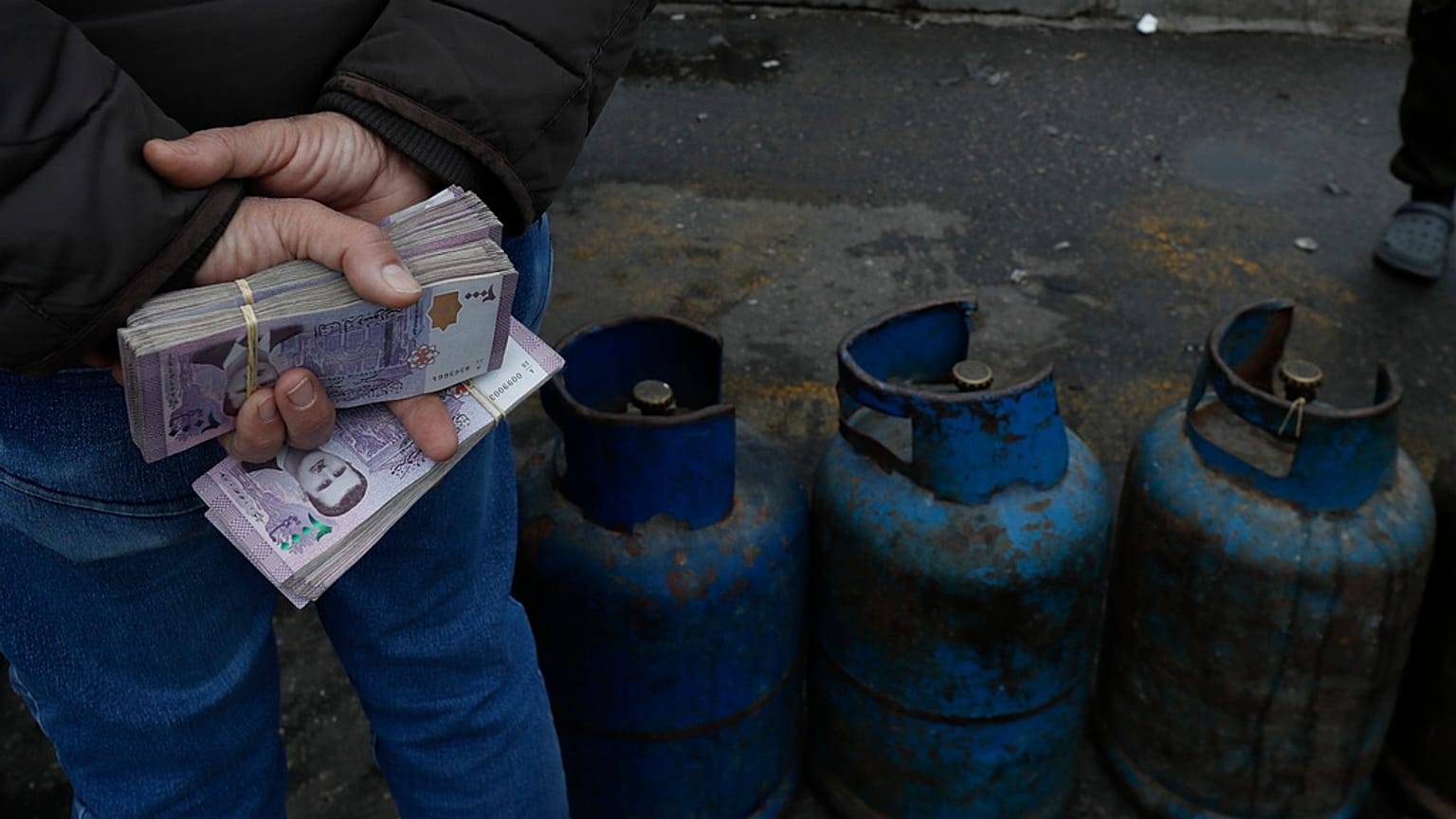 رجل يحمل عبوات من العملة السورية بينما ينتظر شراء الغاز في شارع في الميدان الأموي في دمشق, سوريا, السبت, ديسمبر. 28, 2024.