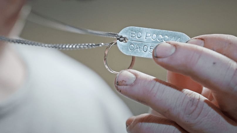 آرش دربندی یک پلاک شناسایی فلزی در دست دارد که به زبان روسی با عبارت «نیروهای مسلح روسیه» مهر شده است