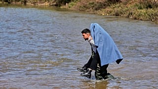  رجل سوري يحمل على ظهره امرأة، أثناء فرارهما من الاشتباكات في سوريا عبر نهر على الحدود بين سوريا وشمال لبنان في منطقة عكار، لبنان  بتاريخ 11 مارس 2025