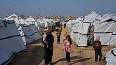 امرأة فلسطينية تحمل طفلاً أثناء سيرها بين خيام أقيمت للنازحين في مدينة غزة، يوم الأربعاء 17 ديسمبر 2025. (تصوير: جيهاد الشرافي/أسوشيتد برس)
