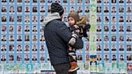 Un hombre sostiene a su hijo en el Muro Conmemorativo de los Defensores de Ucrania Caídos en la Guerra Ruso-Ucraniana y muestra fotos de sus compañeros soldados muertos en Kiev, 25 de diciembre de 2025.