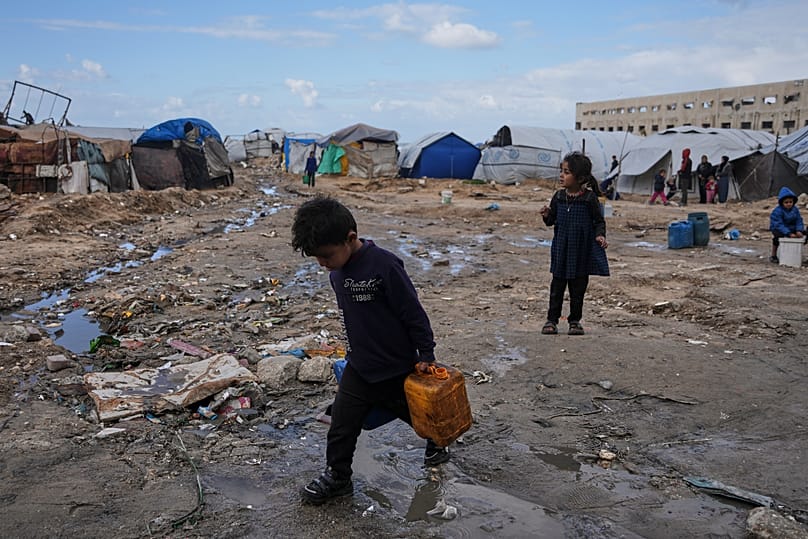 Palestinian children carry plastic jerrycans filled with water as they walk through a displacement camp in Gaza City, 28 December, 2025