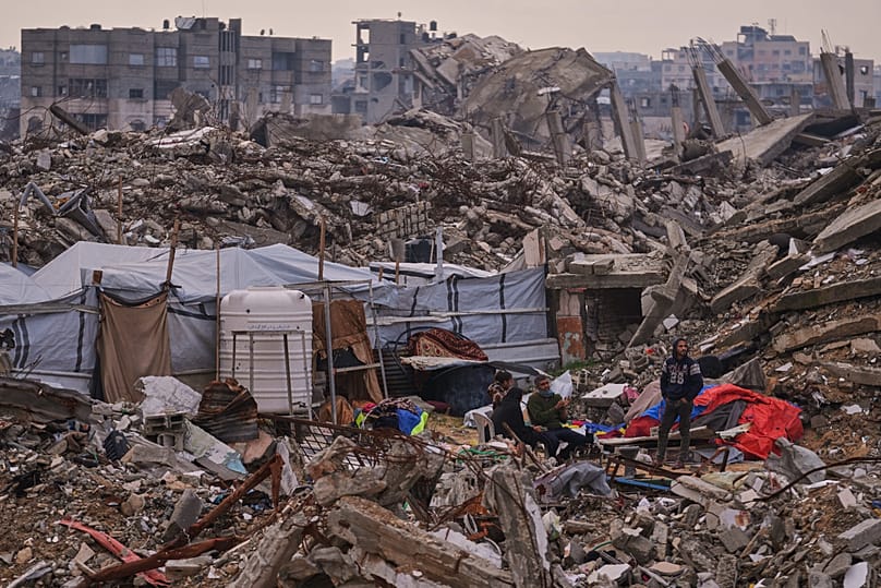 Palestinians stand next to a tent set up on the rubble of buildings destroyed during Israeli air and ground operations in Gaza City, 30 December, 2025