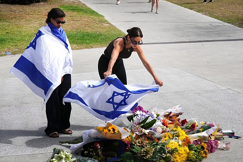 Eine Frau legt eine israelische Flagge auf Blumen vor dem Bondi Pavilion in Sydney – einen Tag nach der Schießerei (15. Dezember 2025).