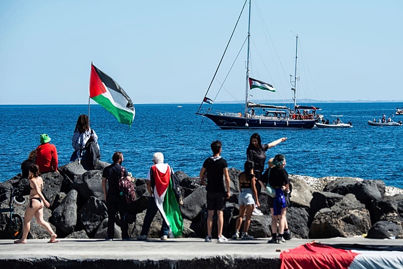 Palesztin zászlóba burkolózó támogatók nézik, ahogy kifut a Freedom Flotilla