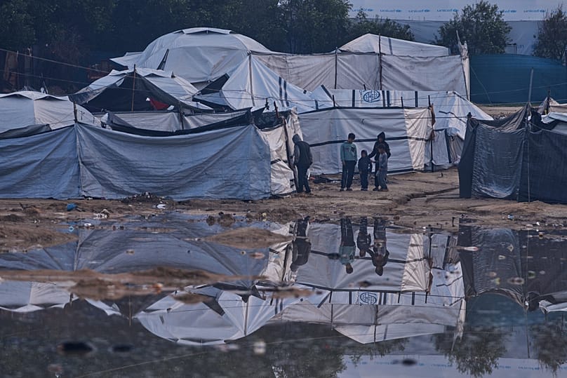 فلسطينيون يقفون قرب منطقة غمرتها المياه بعد أمطار غزيرة في مخيم عشوائي للنازحين في الزوايدة، وسط قطاع غزة، في 17 ديسمبر 2025.