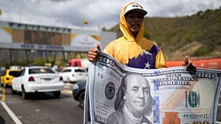 یک فروشنده در ایستگاه عوارضی لا کابرا در جیراردو، ونزوئلا، فرش‌هایی با طرح اسکناس ۱۰۰ دلاری آمریکا را به فروش می‌رساند. این تصویر روز یکشنبه ۲۱ دسامبر ۲۰۲۵ ثبت شده است.