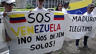 FILE - On 10 January 2019, Venezuelan citizens living in Brazil hold signs that read in Spanish "S.O.S. Venezuela. Don't leave us alone," left, and "Maduro. Illegitimate." 