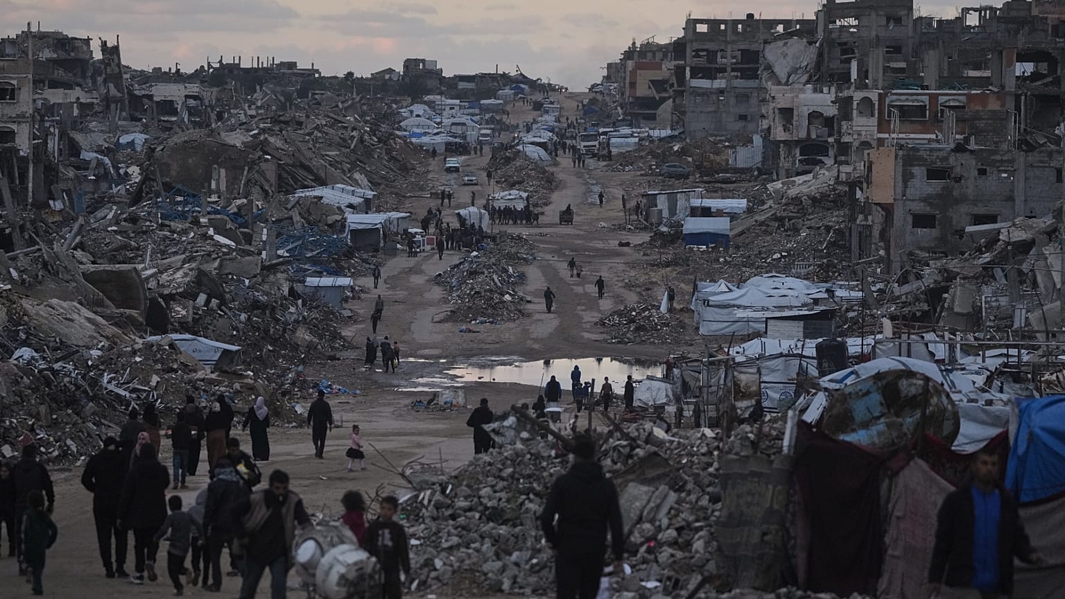 يسير فلسطينيون قرب مبانٍ مدمّرة في شمال قطاع غزة، يوم الجمعة 2 يناير/كانون الثاني 2026.