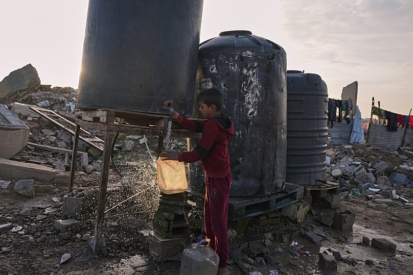 A Palestinian youth collects water from a tank set up in Gaza City, Tuesday, Dec. 30, 2025, amid the rubble of buildings destroyed by Israeli air and ground operations.