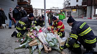 Des pompiers déposent des fleurs près du bar Le Constellation, bouclé, à Crans-Montana, dans les Alpes suisses, en Suisse