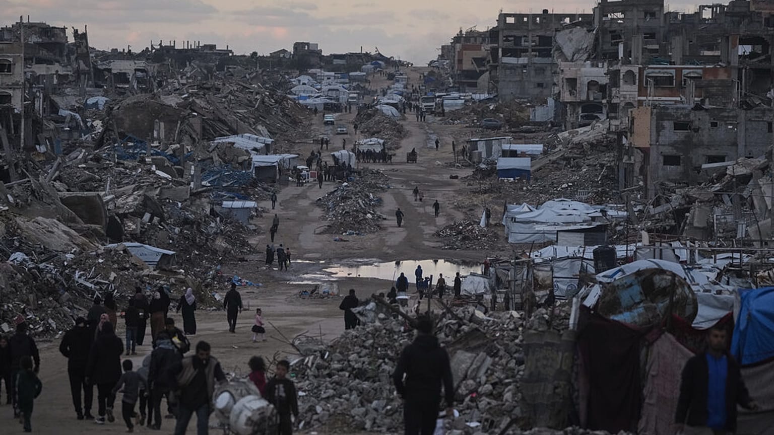 الفلسطينيون يسيرون بجانب مبانٍ مدمرة في شمال قطاع غزة، يوم الجمعة 2 يناير/كانون الثاني 2026.