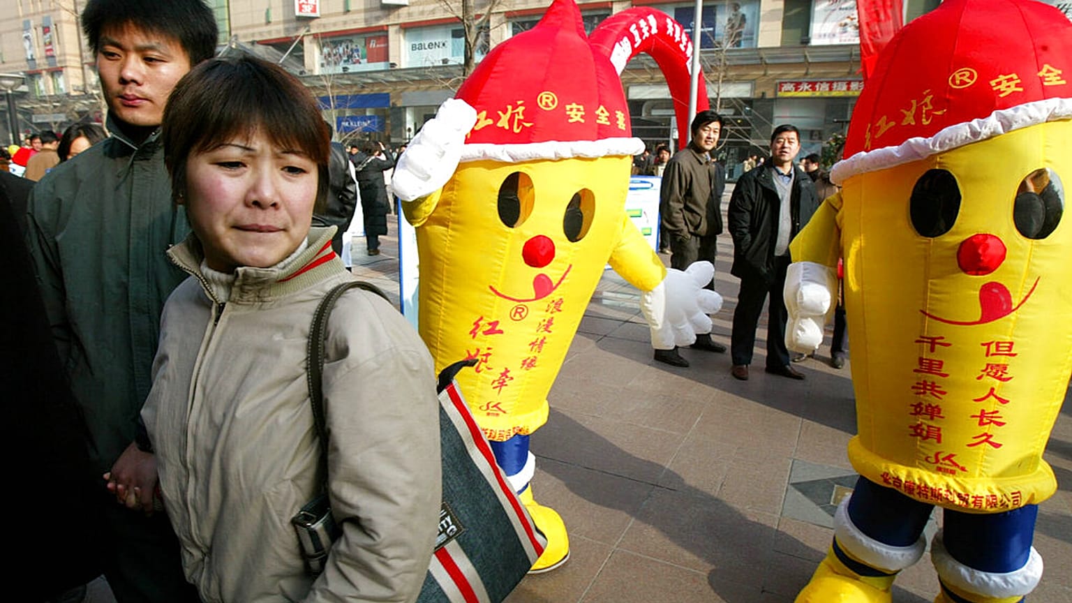 A couple walks past men dressed as condoms at an AIDS awareness activity held in Beijing Saturday, Nov. 29, 2003 ahead of World AIDS Day