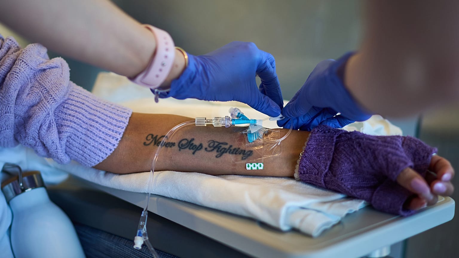 يزين وشم مكتوب عليه "لا تتوقف عن القتال" ذراع روث ويلسون، بينما تتلقى علاجها الوريدي الشهري المخصص لمرض الذئبة في مركز يوماس ميموريال الطبي