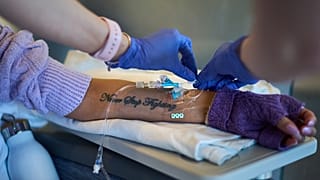 يزين وشم مكتوب عليه "لا تتوقف عن القتال" ذراع روث ويلسون، بينما تتلقى علاجها الوريدي الشهري المخصص لمرض الذئبة في مركز يوماس ميموريال الطبي