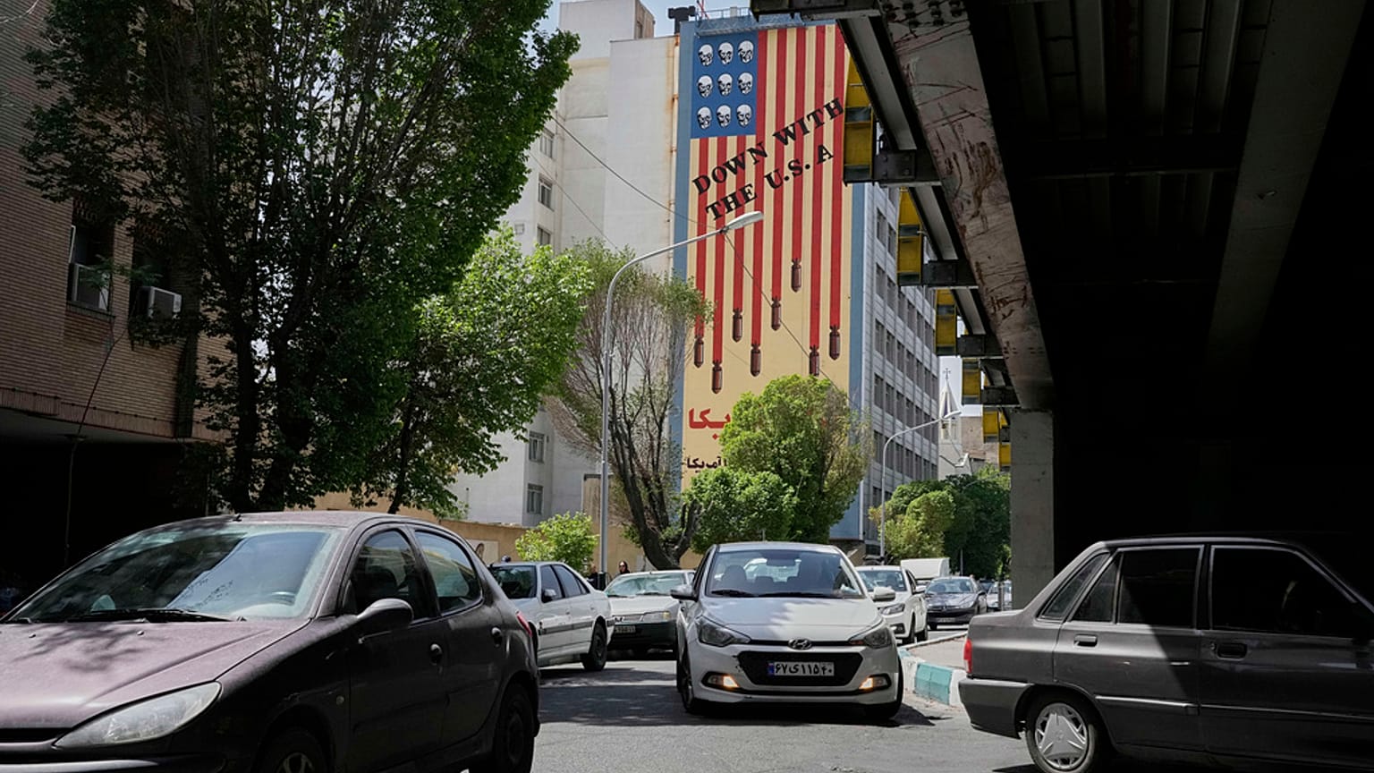  سيارات تسير أمام جدارية مناهضة للولايات المتحدة في وسط مدينة طهران، إيران، الأحد 13 أبريل 2025.