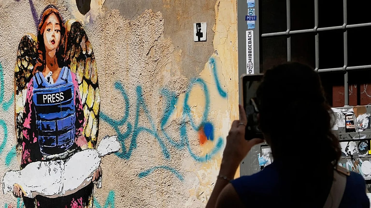 صورة تعبيرية- امرأة تلتقط صورة للوحة "الملاك"، التي رسمها فنان الشارع هاري غريب في وقت سابق من هذا العام، والمخصصة للصحفيين الذين قُتلوا في غزة، وتُظهر ملاكاً يرتدي سترة واقية