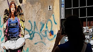 صورة تعبيرية- امرأة تلتقط صورة للوحة "الملاك"، التي رسمها فنان الشارع هاري غريب في وقت سابق من هذا العام، والمخصصة للصحفيين الذين قُتلوا في غزة، وتُظهر ملاكاً يرتدي سترة واقية