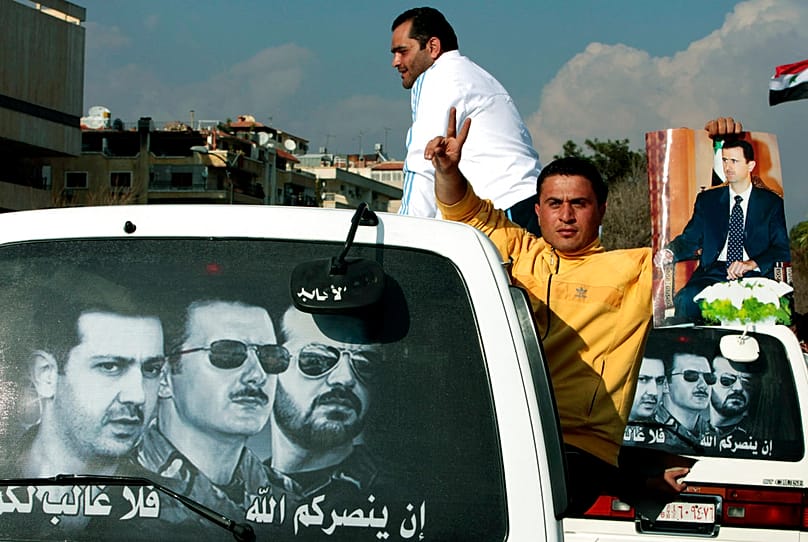 FILE: A man holds a picture of Bashar al-Assad and his brothers Maher and Bassel that says "If God triumphs you, no one can defeat you,” in Damascus, 25 March 2011