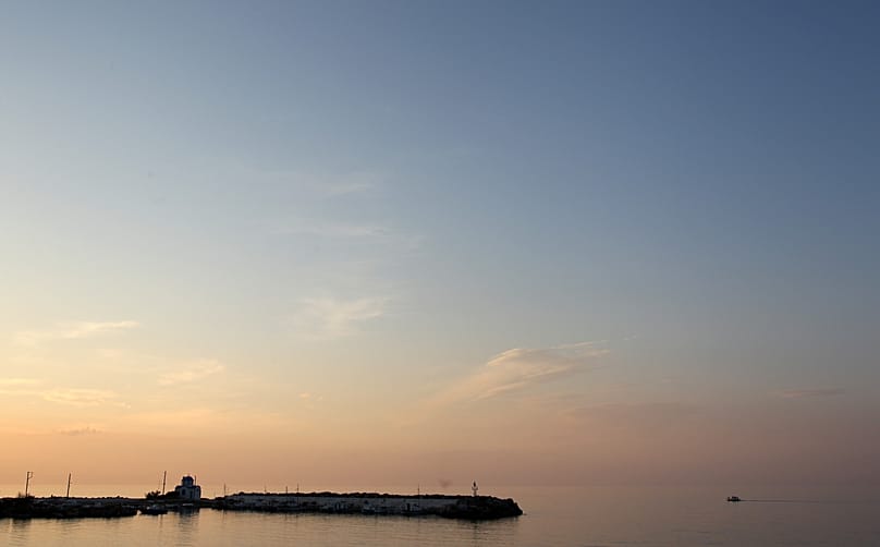 A small fish boat makes its route as a small Greek orthodox church is seen on the port of Gialiskari during the sunset on the Aegean island of Ikaria, northeastern Greece.