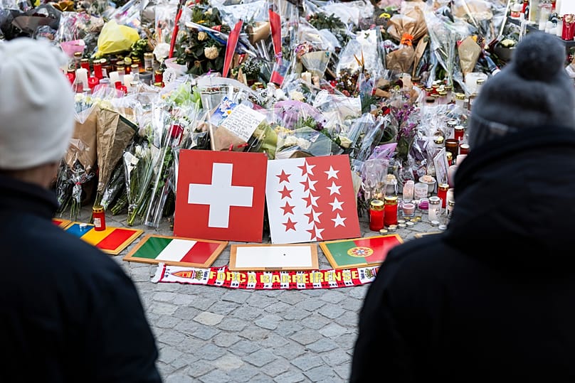 Plaques bearing flags representing Switzerland, Romania, Italy, Portugal, Belgium, France, and Turkey are placed along with flowers and candles to honor the victims