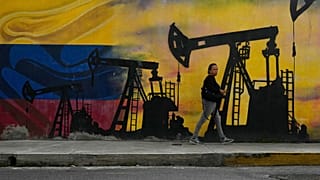 یکی از اهالی کاراکاس، ونزوئلا، در حال عبور از کنار نقاشی دیواری با تصاویر پمپ‌ها و چاه‌های نفت، ۶ ژانویه ۲۰۲۶. 