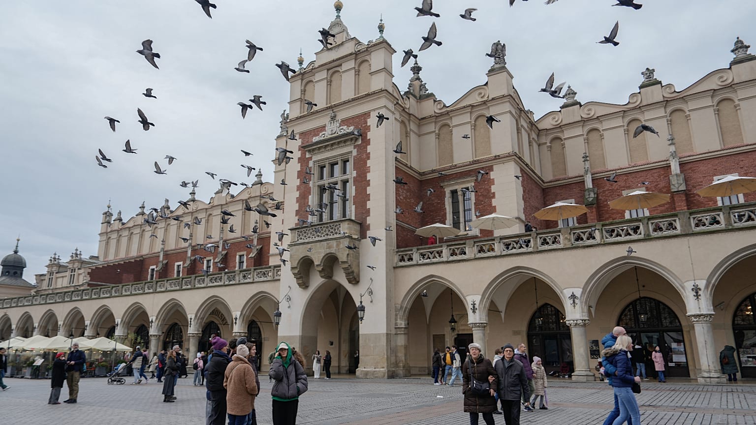Gołębie przelatują nad głowami, a ludzie spacerują po Rynku Głównym w niedzielę, 9 listopada 2025 roku, na Starym Mieście w Krakowie.